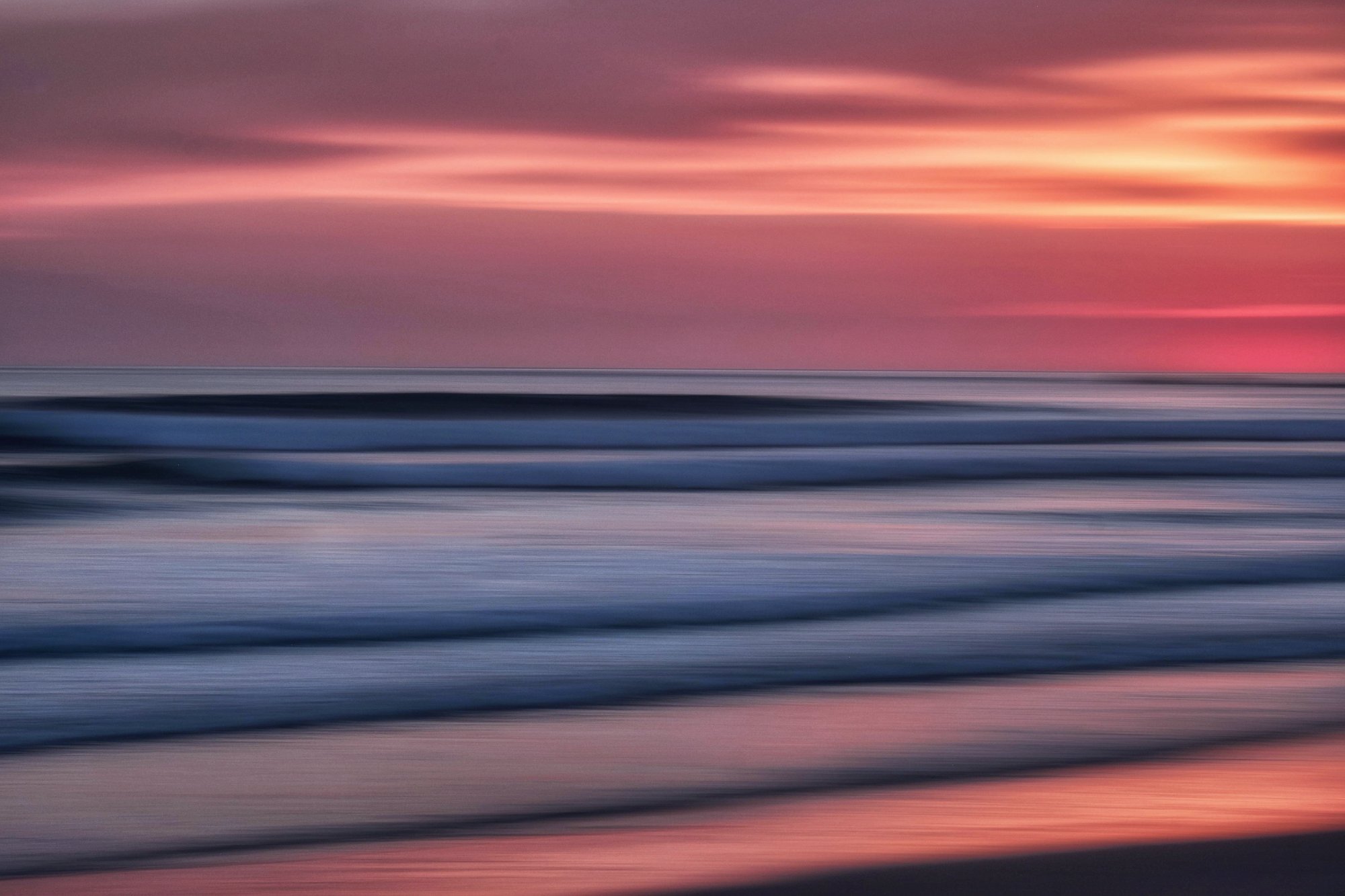 Long exposure ocean waves at sunset, pink and orange sky blending into blue-grey water